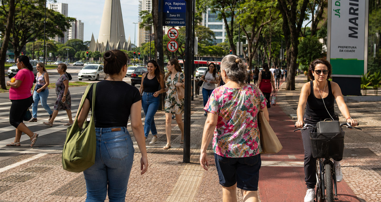 Mulheres caminhando e andando de bicicleta em uma avenida arborizada de Maringá.